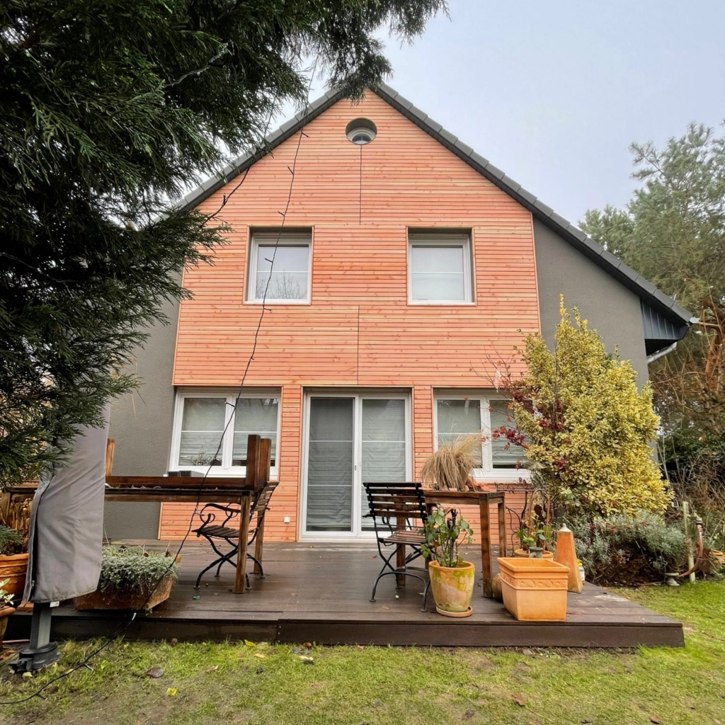 Modernisiertes Einfamilienhaus mit Holzfassade und gemütlicher Terrasse, professionell saniert von KraftBau für langlebige und attraktive Außenbereiche.