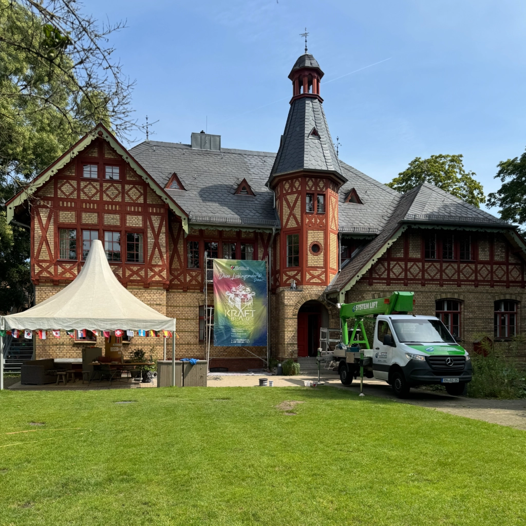 Historische Villa mit Fachwerkfassade, Banner von KraftBau und Hubsteiger, Vorbereitung für Fassadensanierung und Firmenevent im Grünen.