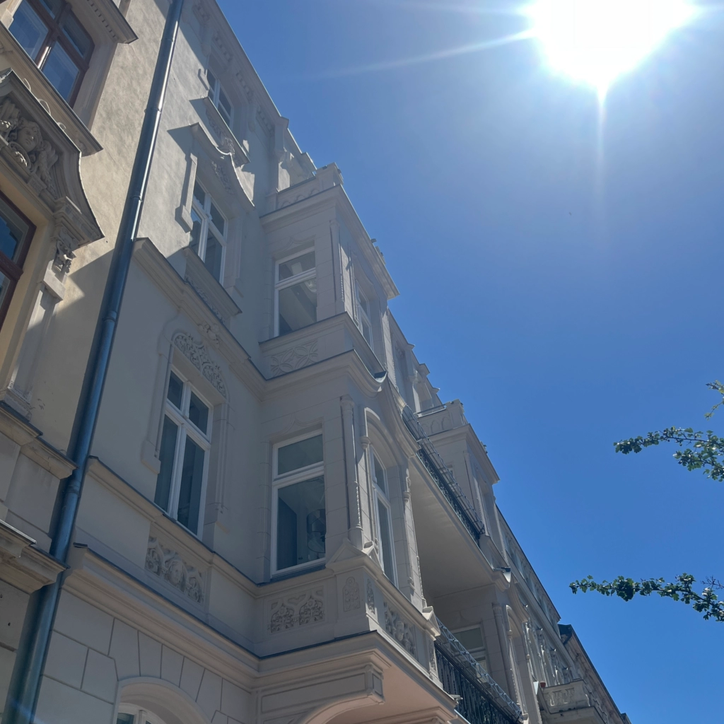 Sanierte Altbaufassade mit Stuckelementen unter strahlend blauem Himmel, professionell restauriert von KraftBau für hochwertige Immobilienaufwertung.