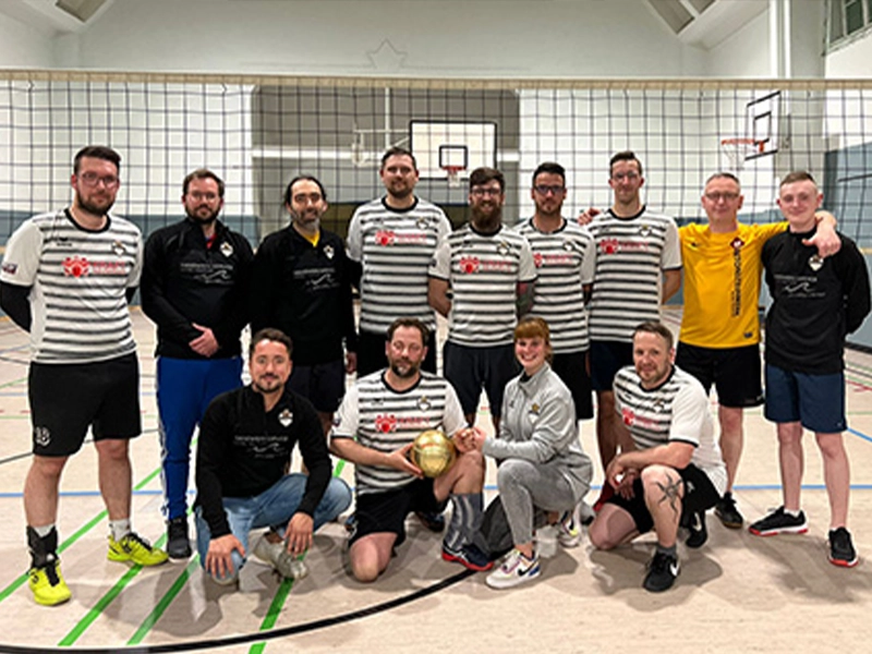 Volleyballteam in Sporthalle, Gruppenfoto mit Pokal, Spieler in gestreiften Trikots und Sponsorenlogo von Kraft Bau.