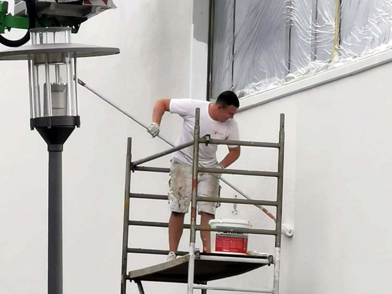 Fassadenmaler von KraftBau beim Streichen einer Hauswand auf einem Gerüst, präzise Handwerksarbeit für hochwertige Außenanstriche.