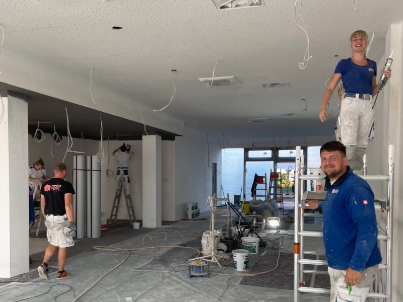 Team von KraftBau bei der Renovierung eines Innenraums, Maler und Handwerker bei Deckenarbeiten und Vorbereitungen für moderne Innenausbauten.
