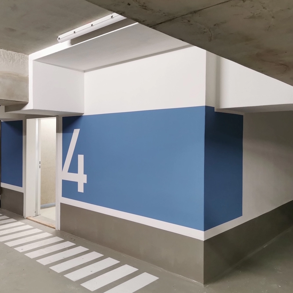 Frisch gestrichene Tiefgarage mit blauer Wandmarkierung und großer Zahl 4, professionell umgesetzt von KraftBau für klare Orientierung und modernes Erscheinungsbild.