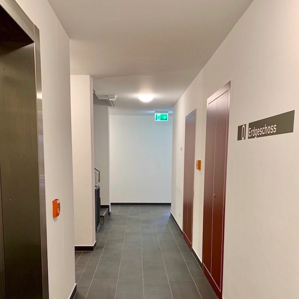 Modern gestalteter Hausflur im Erdgeschoss mit Aufzug, Beschilderung und Fliesenboden, renoviert von KraftBau für gepflegte und funktionale Innenbereiche.